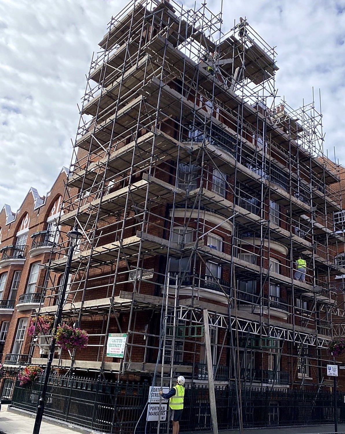 Corner scaffold on a red brick London mansion block with a scaffolder at street level
