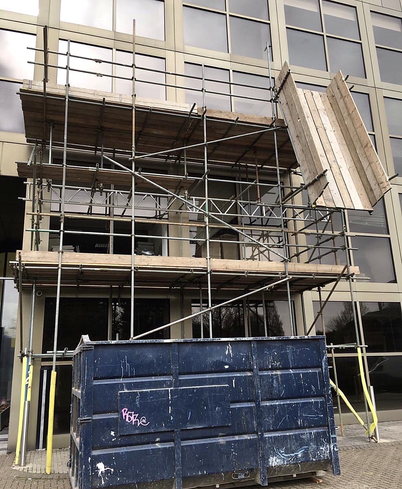Access scaffold and loading platform over a glass office entrance with a skip below