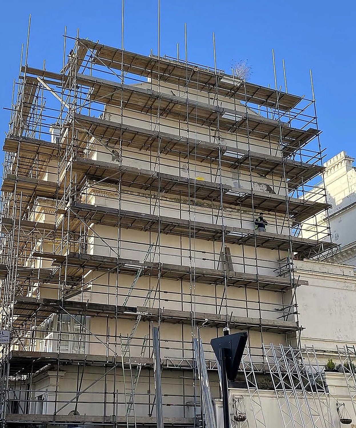 Full scaffold wrap around a large white stucco building with boarded lifts