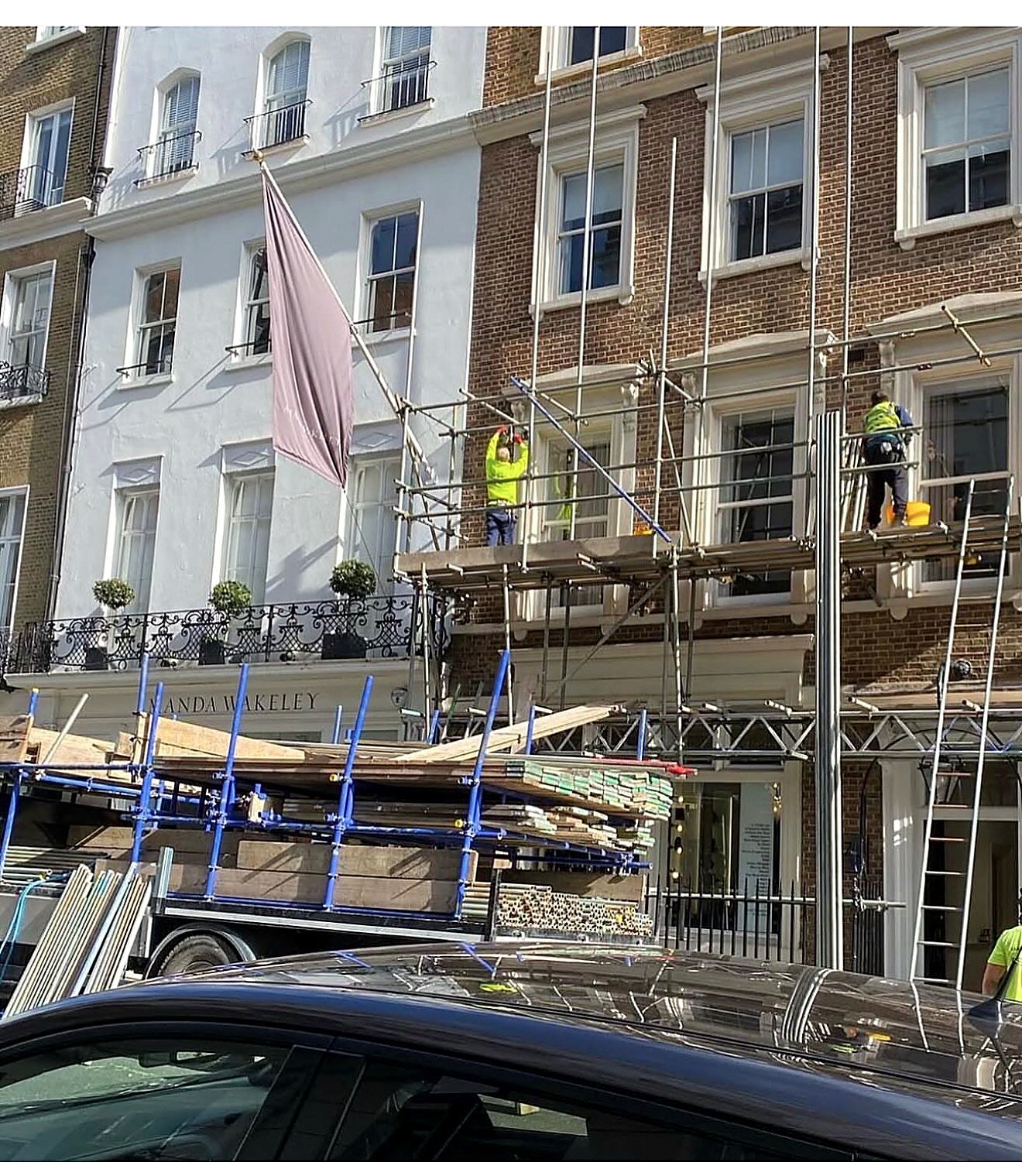 Scaffolders working on a boarded lift outside a white stucco townhouse while the lorry is unloaded